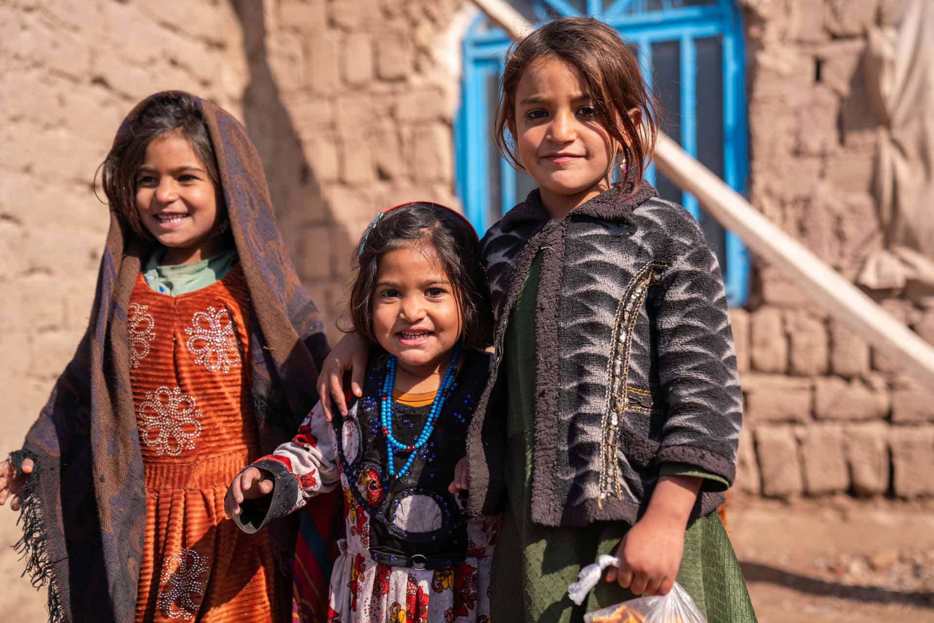 Afghani girls Malayeka and her sister Maryam stand in front of their mud brick home 