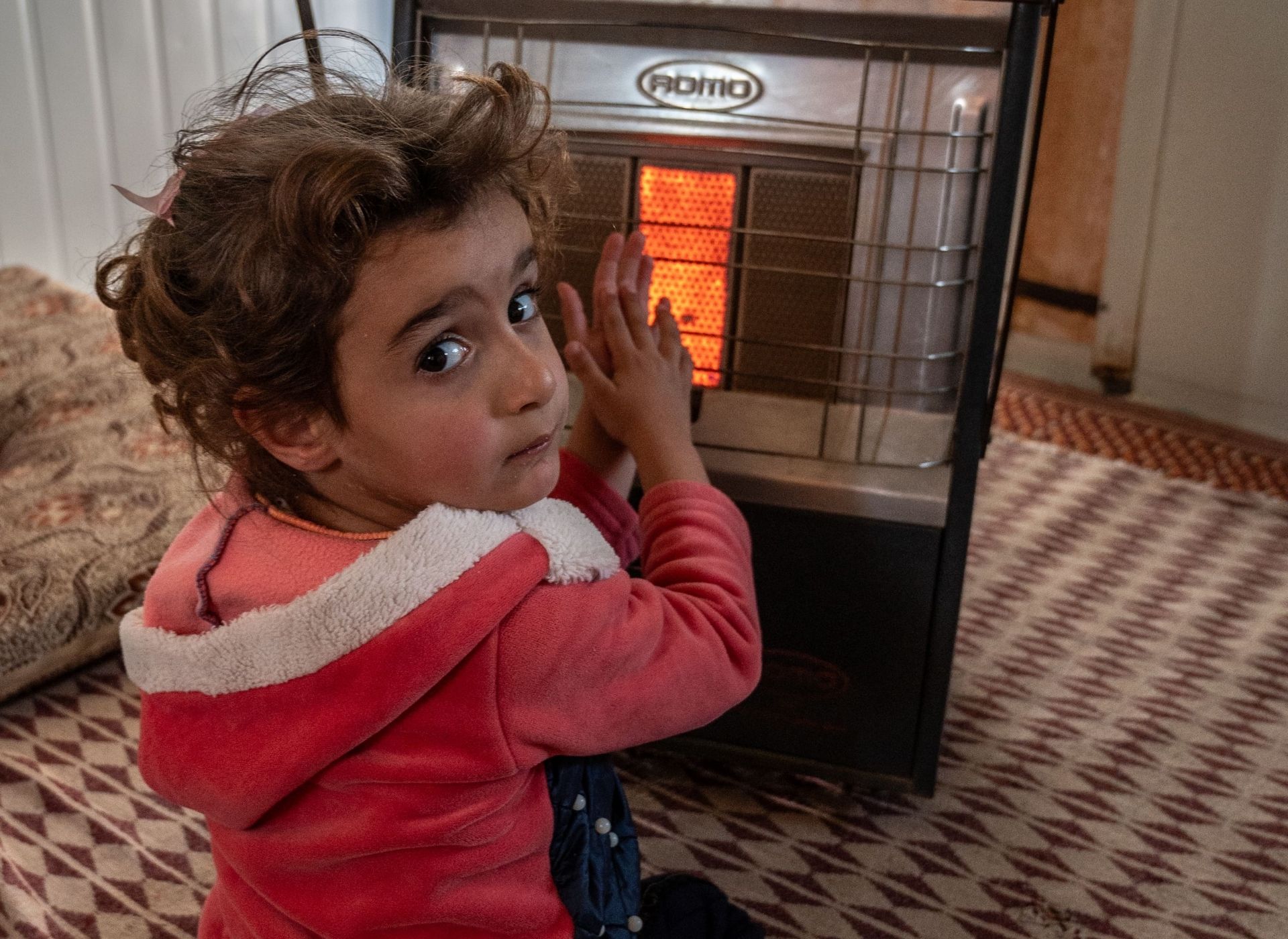 Emarat, a five-year-old Syrian girl, warms herself in front of her family's gas heater in their shelter in Za'atari refugee camp, Jordan.