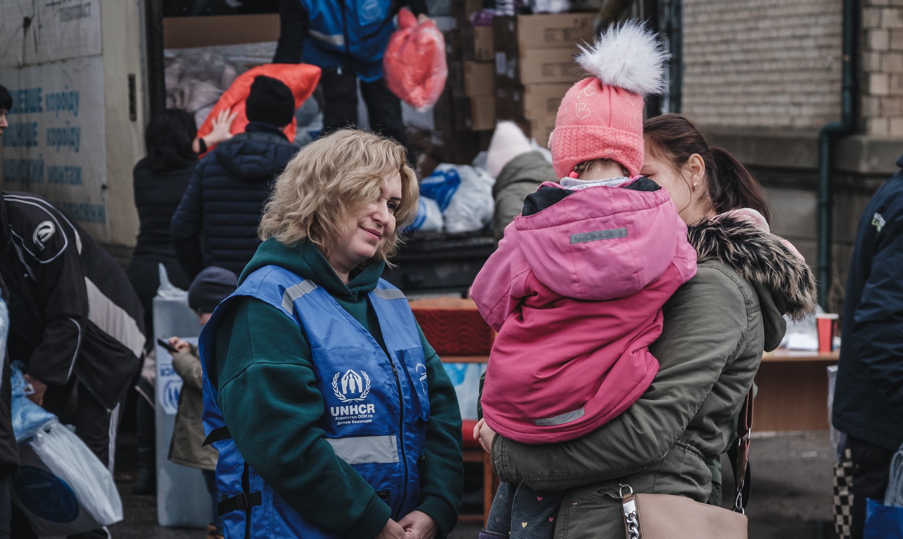 A UNHCR staff member talks to a woman holding a child near an aid distribution point