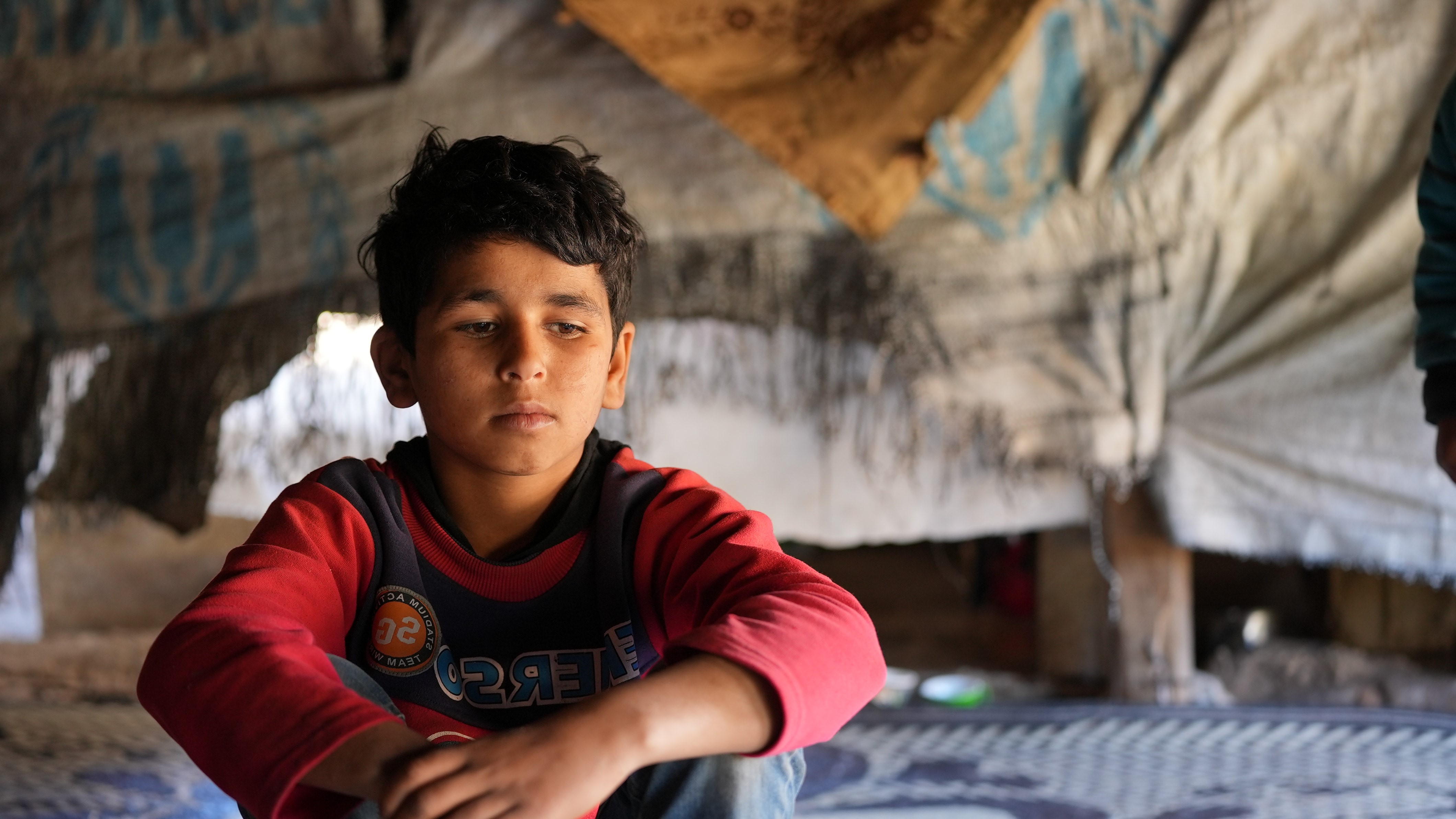 13 year old Azzam plays with marbles inside and outside his tent. 