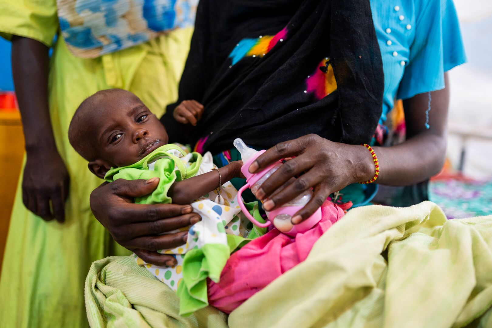 Baby held in a woman’s arms while she feeds the infant with a bottle of milk