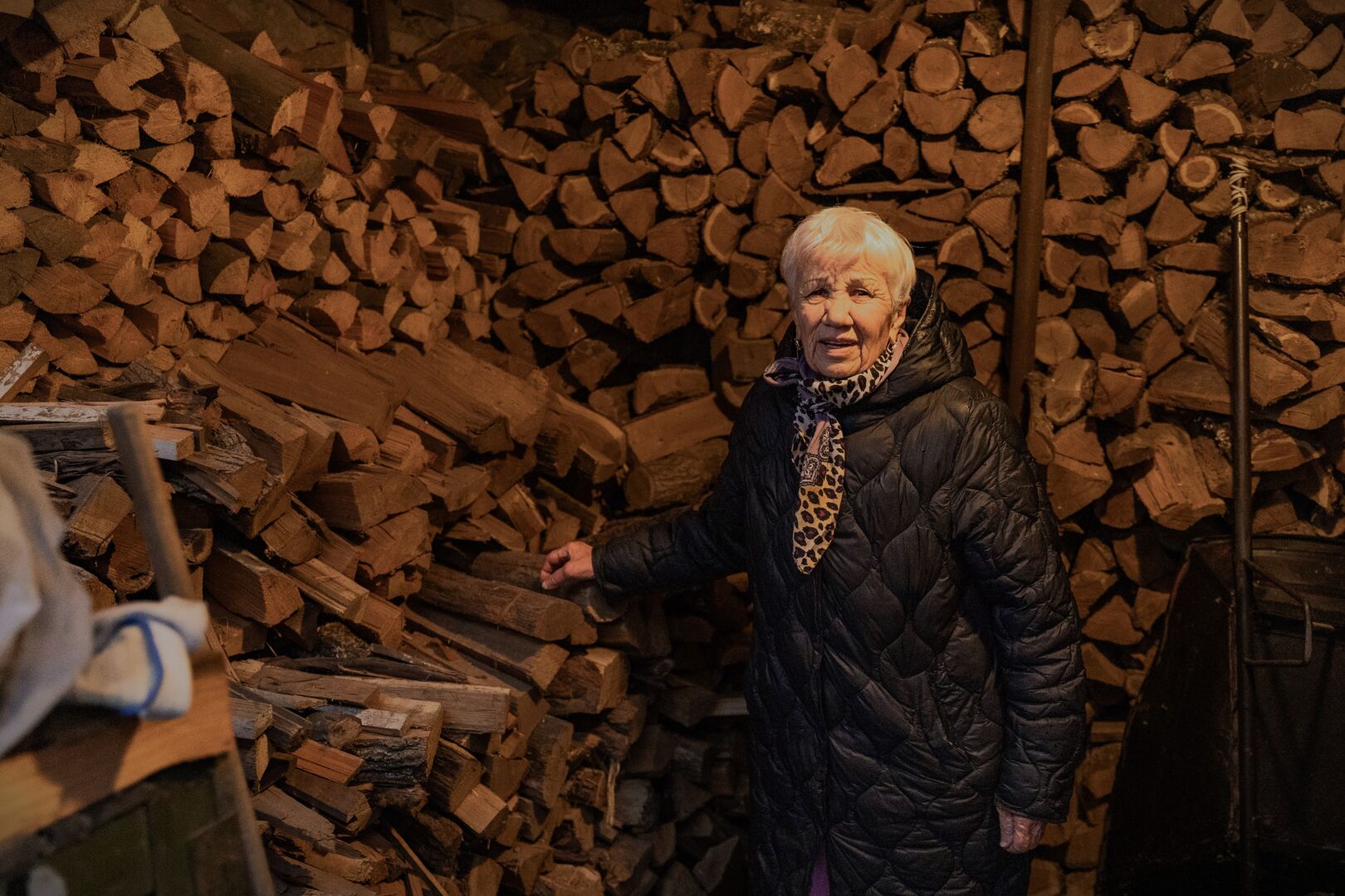 Ievhenia stands in front of stacked firewood, which she purchases with UNHCR cash assistance to help her stay warm during winter.